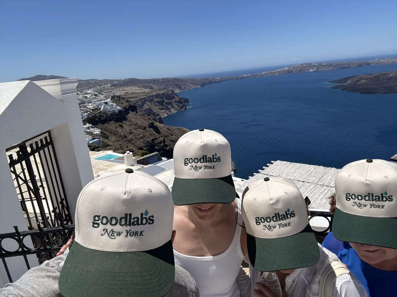 Four friends in Goodlabs New York hats overlooking the Santorini caldera